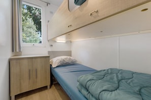 Ein kleines Zimmer mit einem Einzelbett, einem kleinen Holzschrank und einem Fenster.
