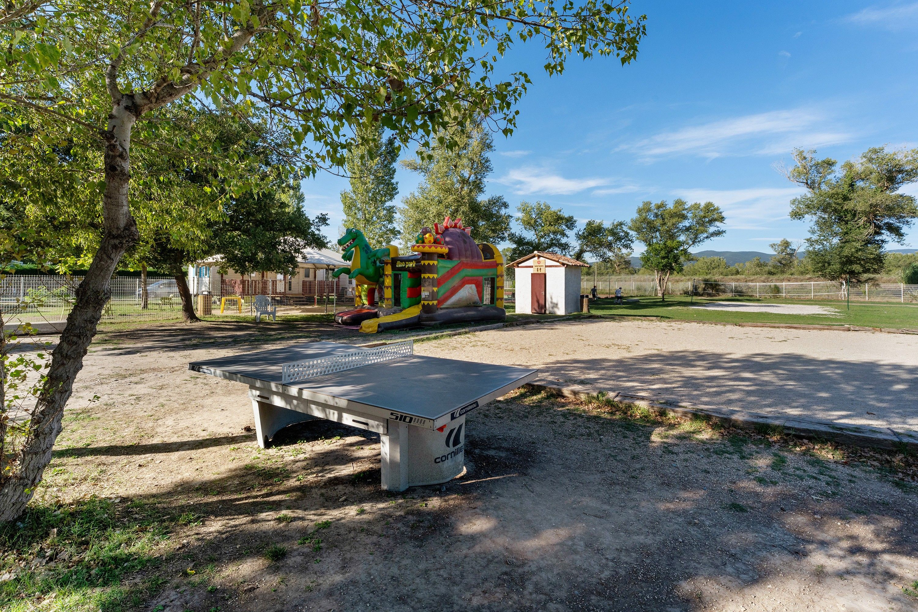 Un terrain de jeux équipé d’une table de ping-pong, de structures gonflables et d’un petit bâtiment.