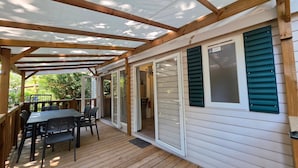 Ein überdachter Außenbereich mit Holzterrasse, einem Tisch mit Stühlen und einer Schiebetür zu einem Zimmer.