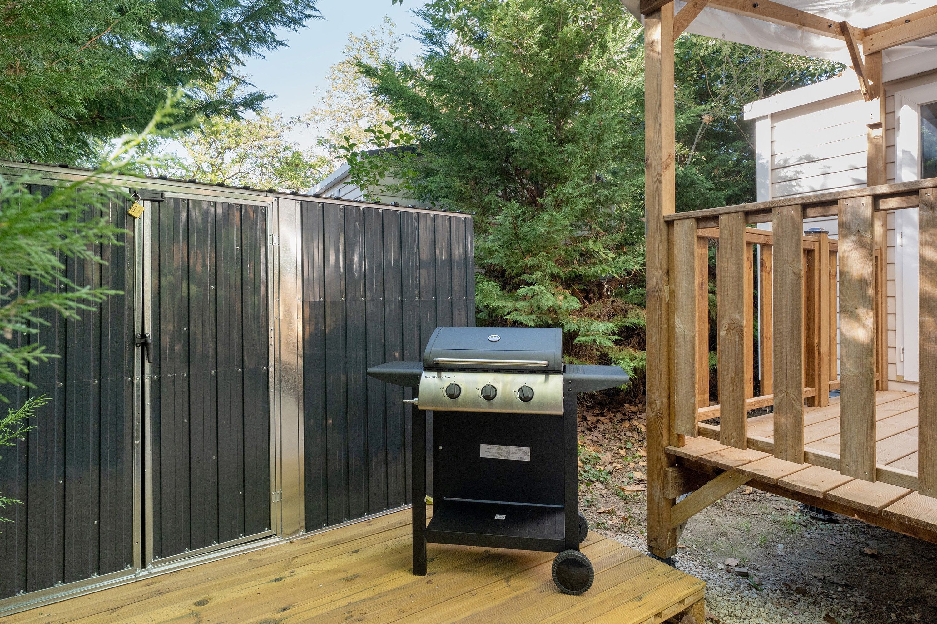 Una parrilla para barbacoa en una terraza de madera, con una valla y una estructura de madera al fondo.