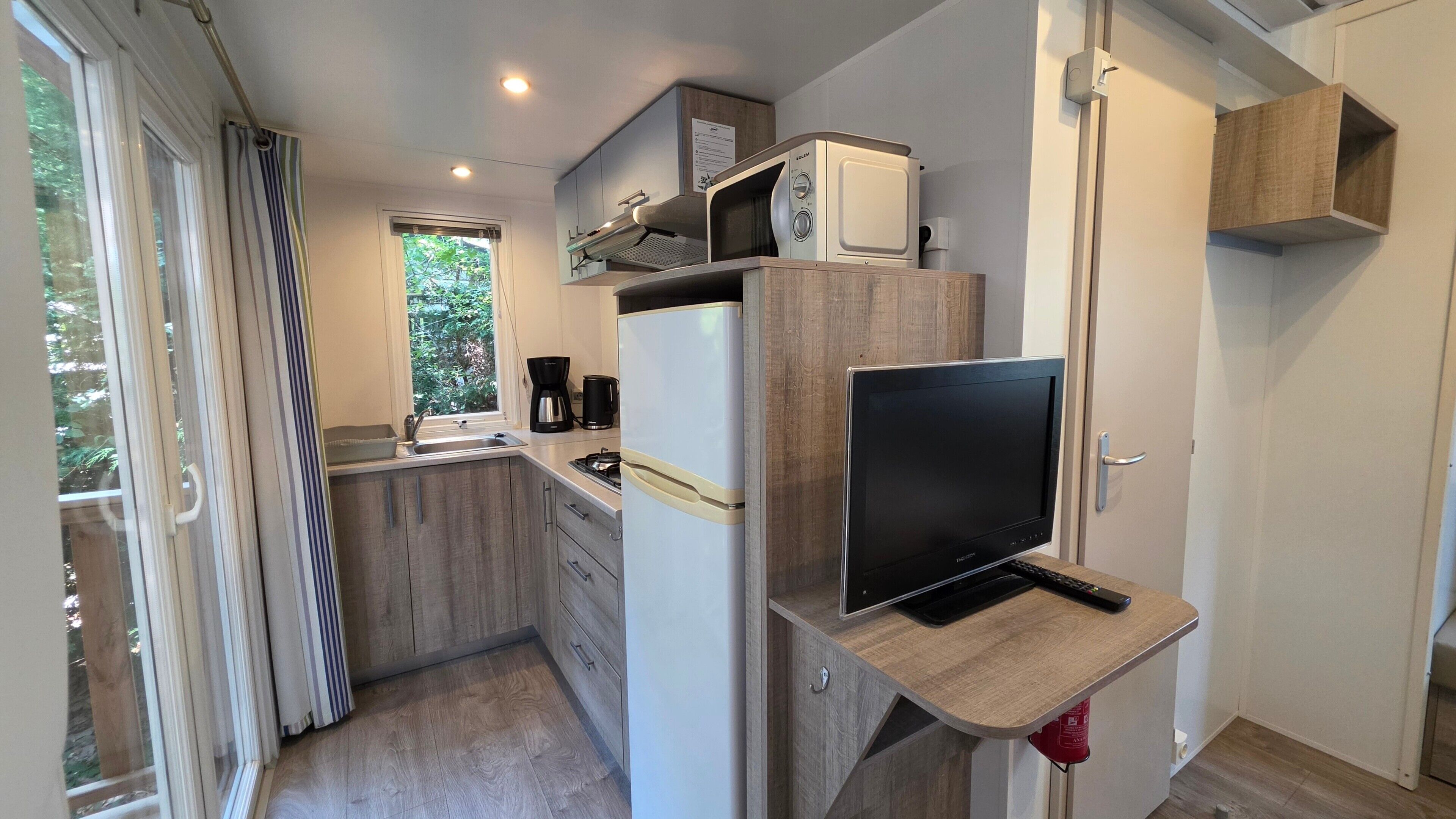 Een praktische keuken met een ingebouwde magnetron, een fornuis, een spoelbak en een flatscreen televisie.