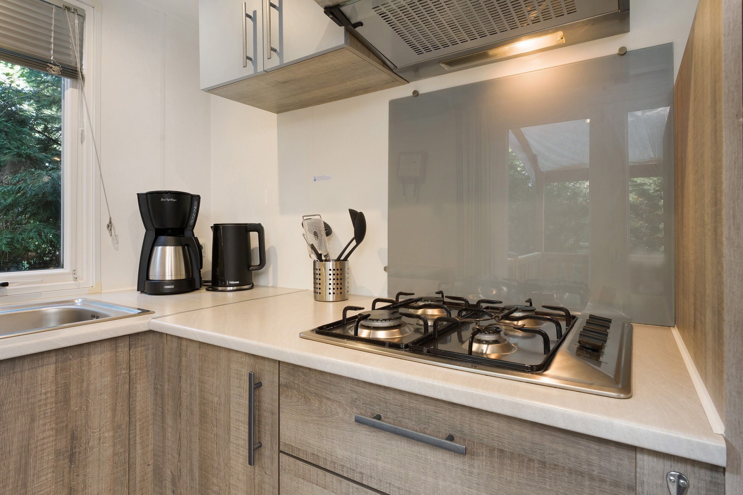 Una cocina moderna con estufa a gas, cafetera y una ventana con persianas.