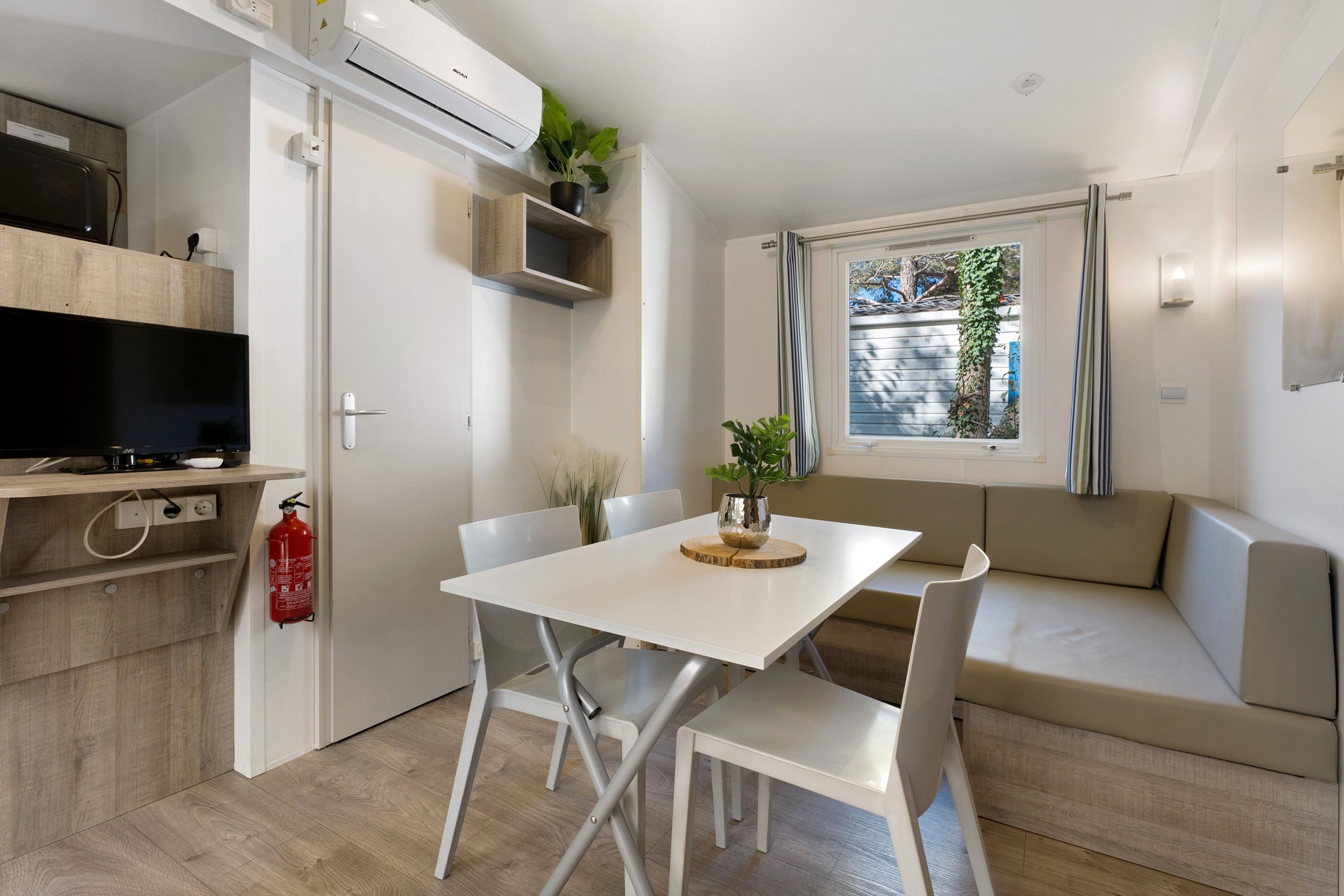 Una kitchenette compacta con horno empotrado, una mesa de comedor con sillas y un sofá con vistas al exterior.