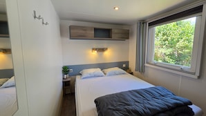 Ein Hotelzimmer mit Bett, Nachttischen, einer kleinen Ablage, einem Fenster mit Vorhängen und einer Wandleuchte.