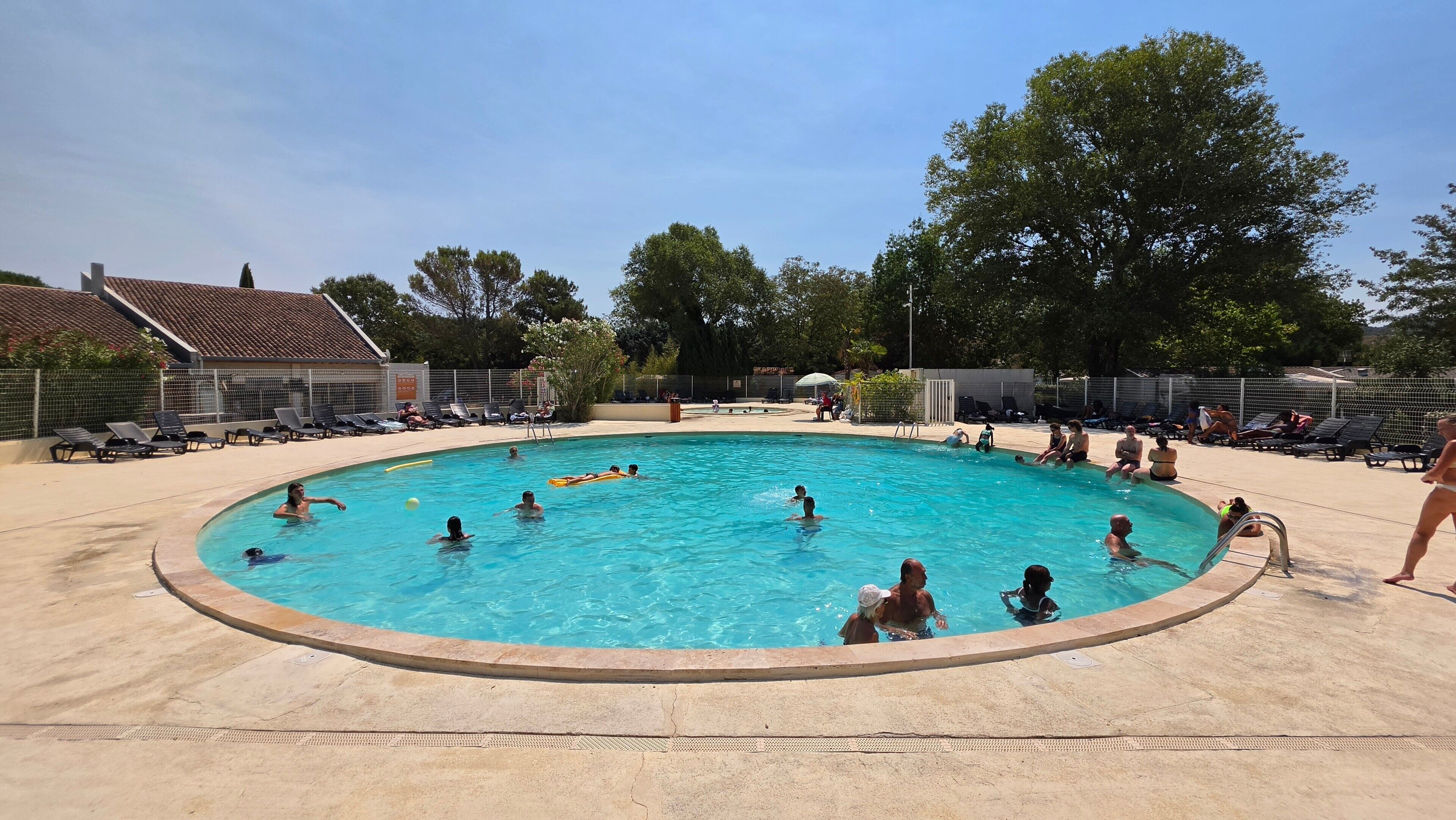 Ein Swimmingpool, umgeben von Liegestühlen und einem von Bäumen gesäumten, eingezäunten Bereich.