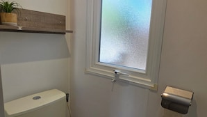 Ein kleines Badezimmer mit Toilette, einem Fenster und einem Regal über der Toilette.