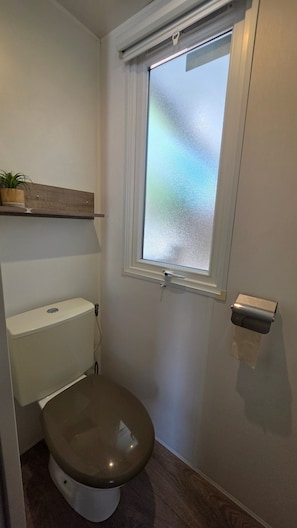 Ett litet badrum med en toalett, ett fönster och en hylla ovanför toaletten.