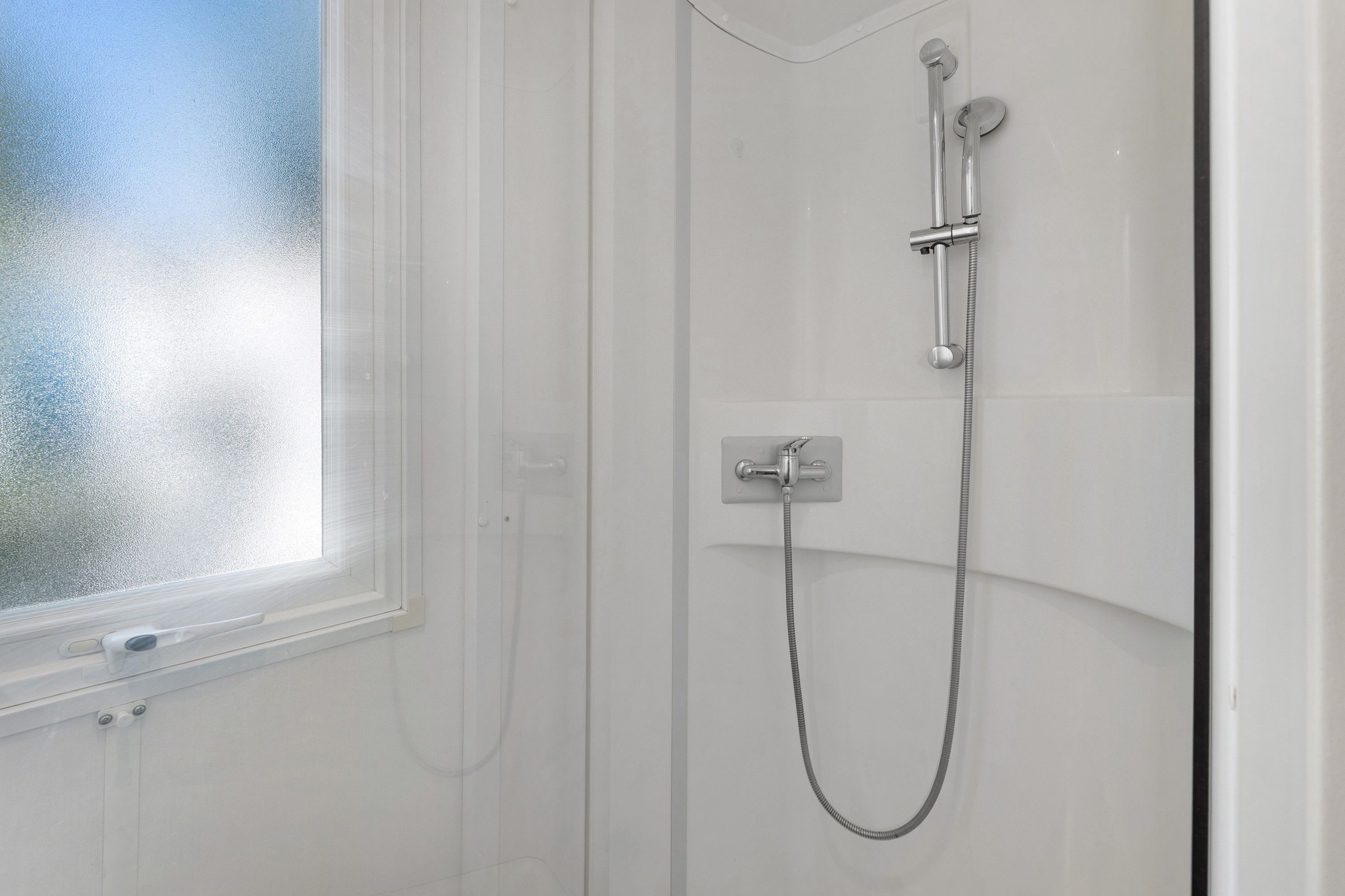 Une salle de bain avec une douche, une fenêtre et un panneau de commande fixé au mur.