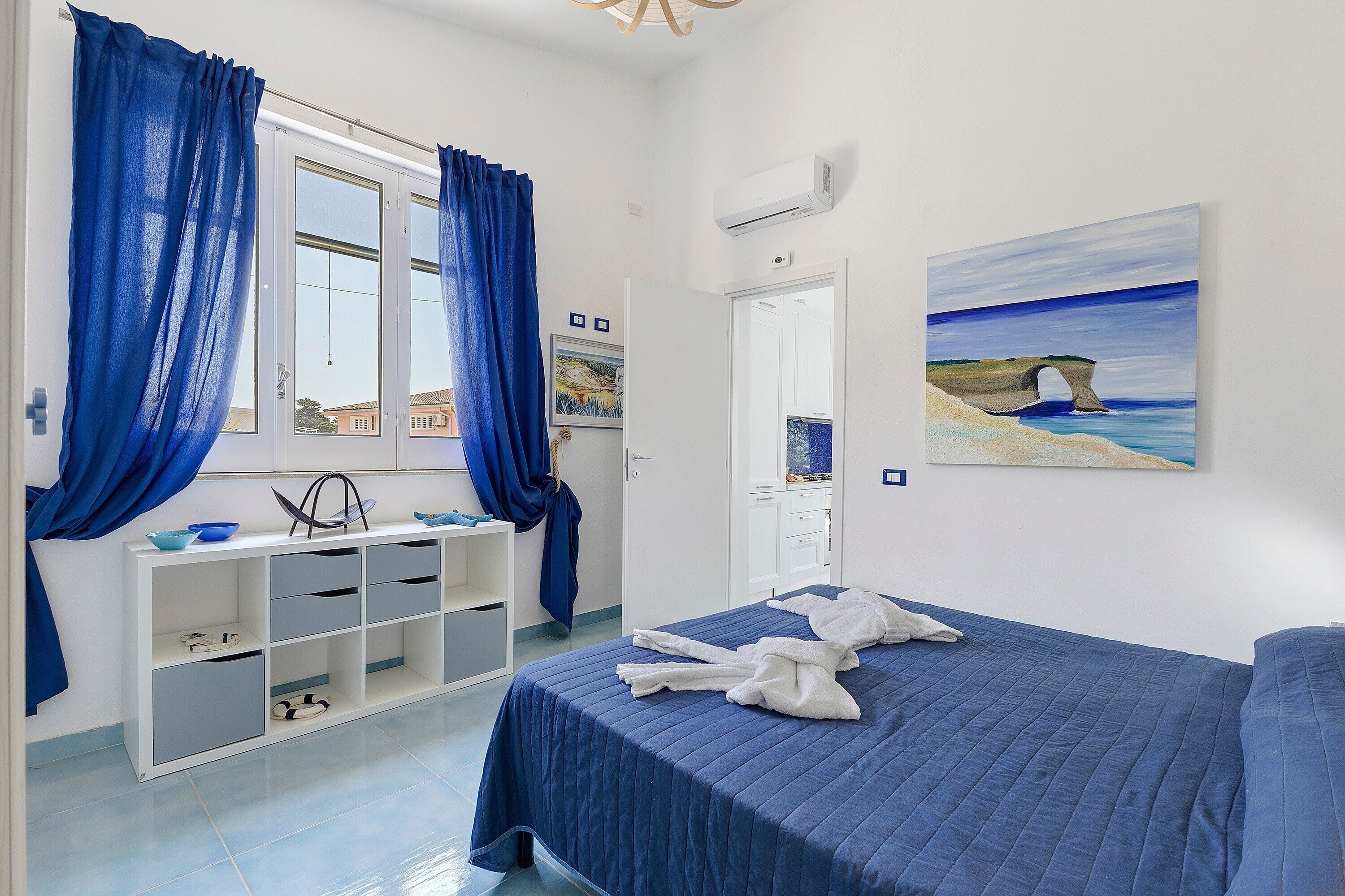Una camera da letto con un letto, una scrivania con cassetti, una finestra con tende, un condizionatore d'aria e un quadro appeso al muro.