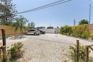 A gravel driveway leading to a garage with parked cars, surrounded by a wooden fence and vegetation.
