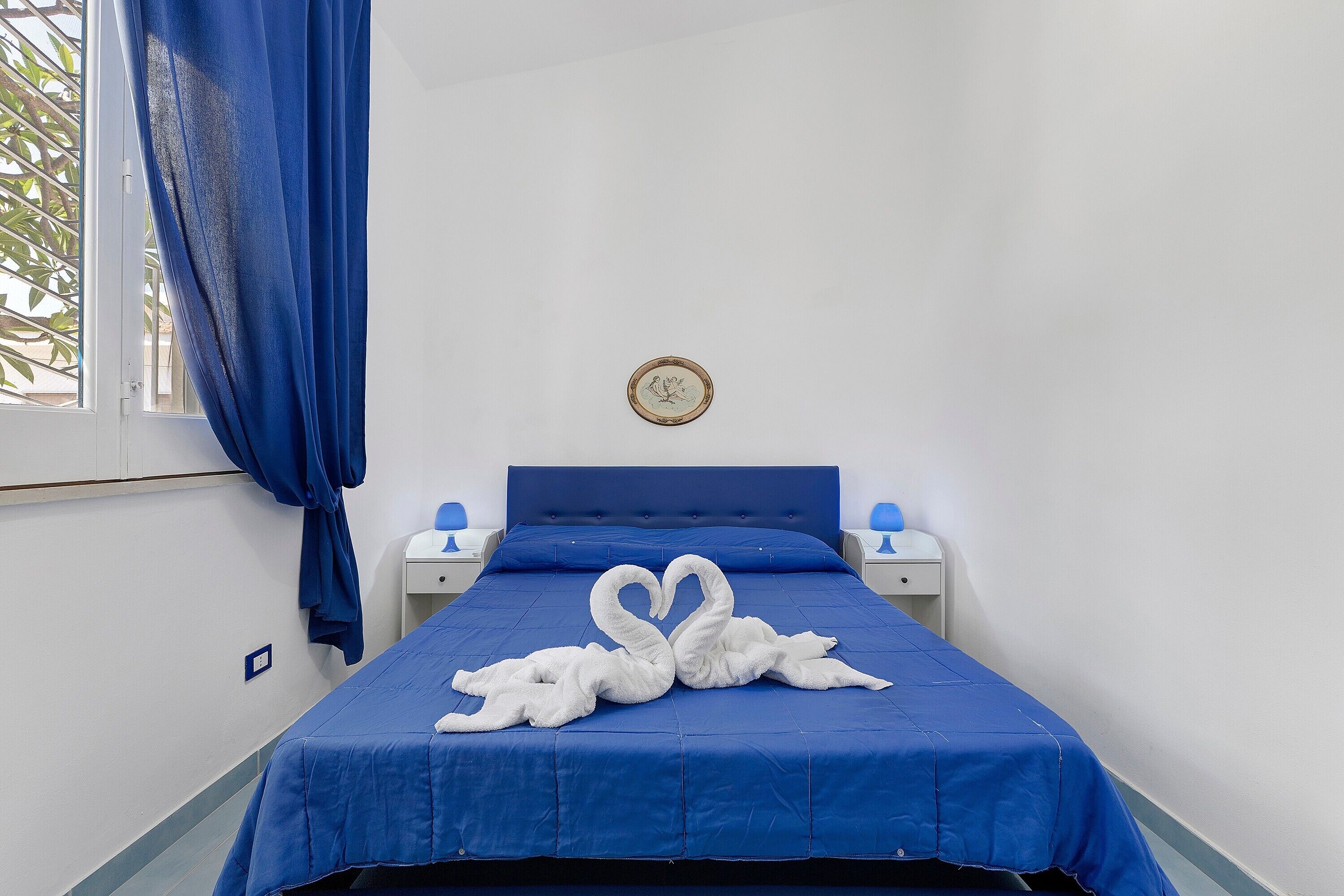 Ein Einzelbett mit blauer Bettdecke und zwei weißen Handtüchern, die zu einem Herz geformt sind.