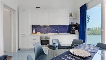 Una cucina moderna con mobili bianchi, una parete di sfondo blu e un'area pranzo con un tavolo e sedie in vetro.
