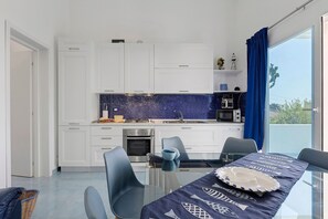 A modern kitchen with white cabinets, a blue backsplash, and a dining area with a glass table and chairs.