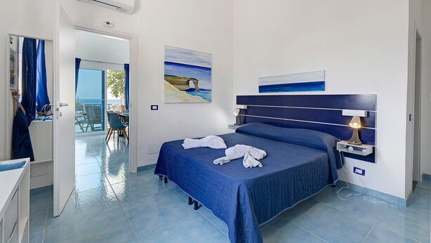 A hotel room with a bed, a desk, and a view of the sea through the window. - Villa Pomelia - just steps from the sea (Pozzallo)