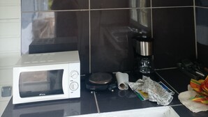 Keittiössä on valkoinen mikroaaltouuni, kahvinkeitin ja erilaisia keittiötarvikkeita työtasolla.