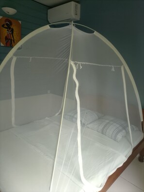 A bed with a mosquito net, a wall-mounted air conditioner, and a painting on the wall. - 🌴 Your little corner of paradise on the Caravelle Peninsula (La Trinité)