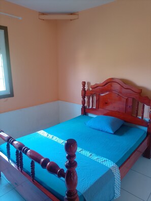 Una habitación con una cama de madera, una colcha azul y una ventana.
