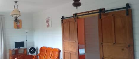 A room with a wooden chair, a table, a TV, and a ceiling fan.