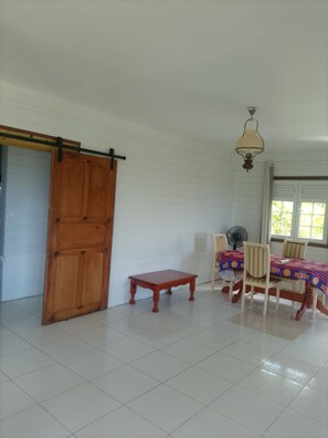 A room with a sliding door, a small table, a dining table with chairs, a ceiling fan, and a window with blinds. - 🌴 Your little corner of paradise on the Caravelle Peninsula (La Trinité)