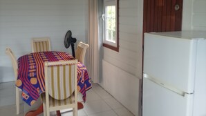 A small room with a dining table, chairs, a refrigerator, and a window with curtains. - Vrbo Property (La Trinité)