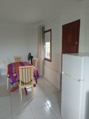 Una habitación pequeña con una mesa, sillas, un refrigerador y un ventanal con cortinas.