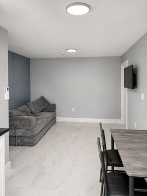 A modern living space with a grey sofa, a dining table with chairs, and a flat-screen TV mounted on the wall. - Phenomenal 1-bedroom apartment with AC in Wilton Manors (Wilton Manors)