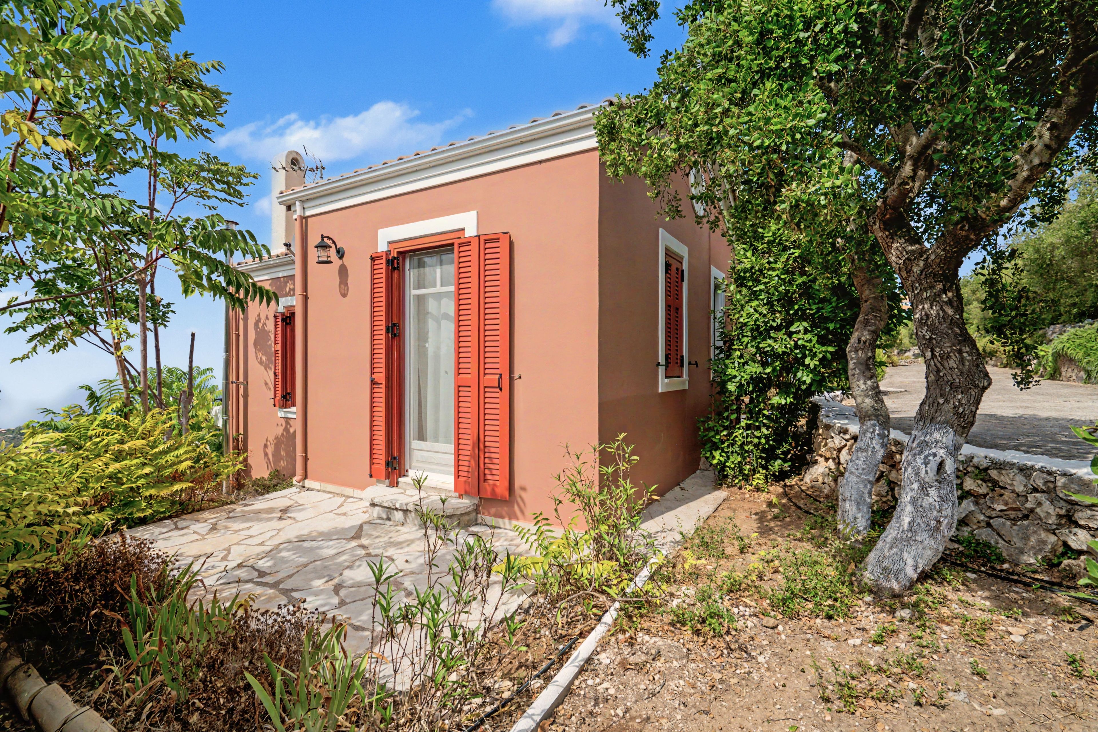 A small building with a stone-paved entrance, red shutters, and a clear sky.