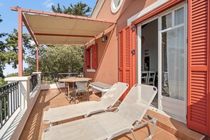 A balcony with two lounge chairs, a table, and chairs, a covered area, and a sliding glass door. - Holiday Home 'Villa Meltemi' with Sea View, Wi-Fi, and Air Conditioning (Tsoukalades)