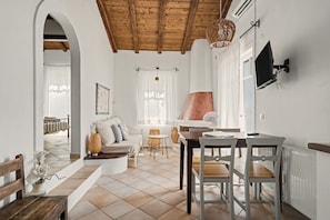 A spacious living area with a high ceiling, a fireplace, a dining table with chairs, and a television mounted on the wall. - Holiday Home 'Villa Meltemi' with Sea View, Wi-Fi, and Air Conditioning (Tsoukalades)