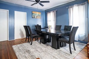 Une salle à manger avec une table et des chaises noires, un ventilateur de plafond et un tableau accroché au mur.