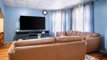 Una sala de estar con televisor de pantalla plana, sofá de cuero y un reloj en la pared.