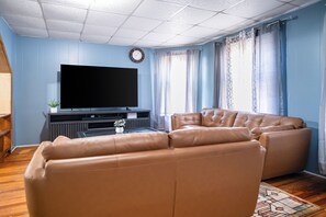 Een woonkamer met een flatscreen televisie, een leren bank en een klok aan de muur.
