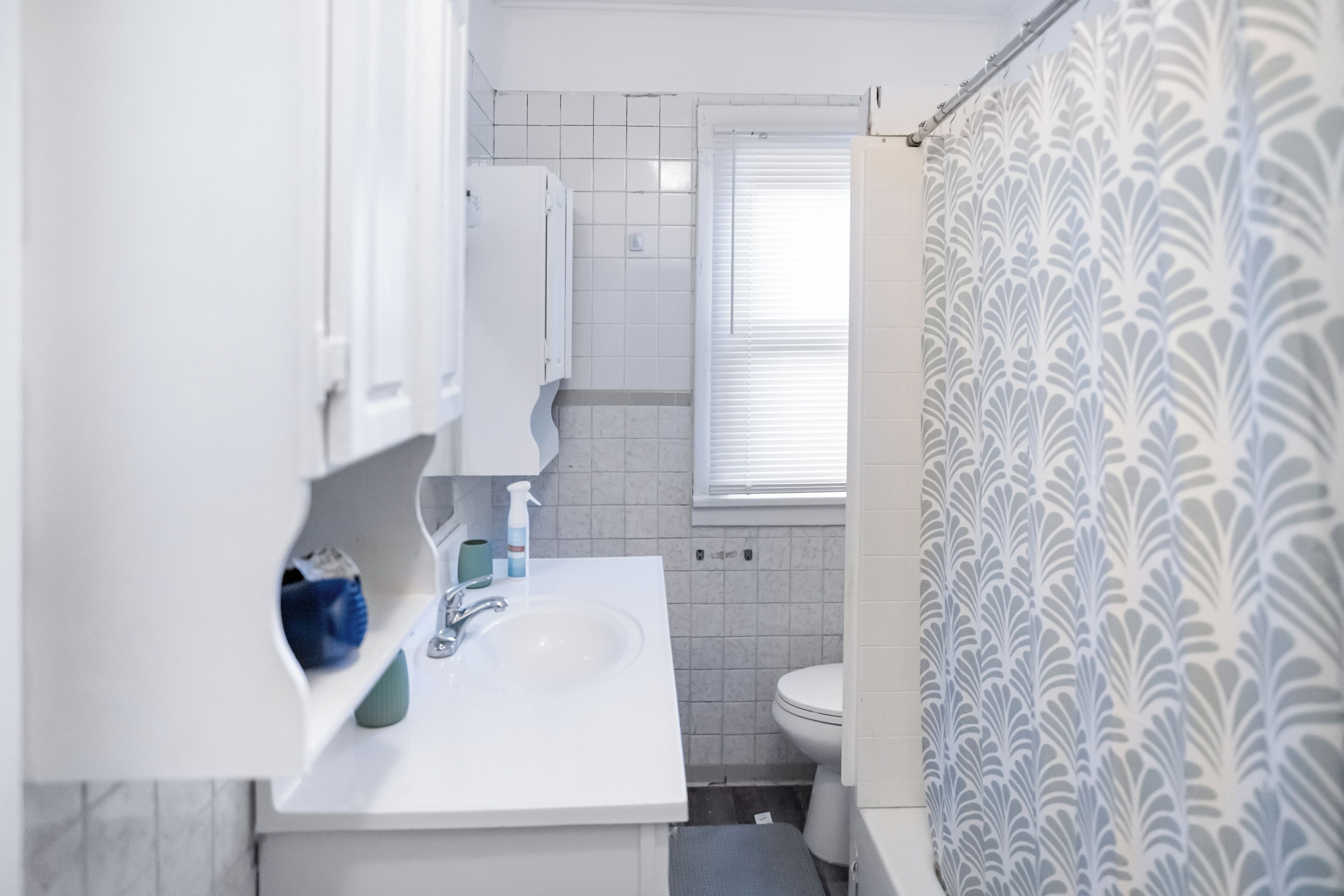 Ein Badezimmer mit einem weißen Waschbecken, einem Spiegel, einer Toilette und einem Duschvorhang mit Blättermotiv.