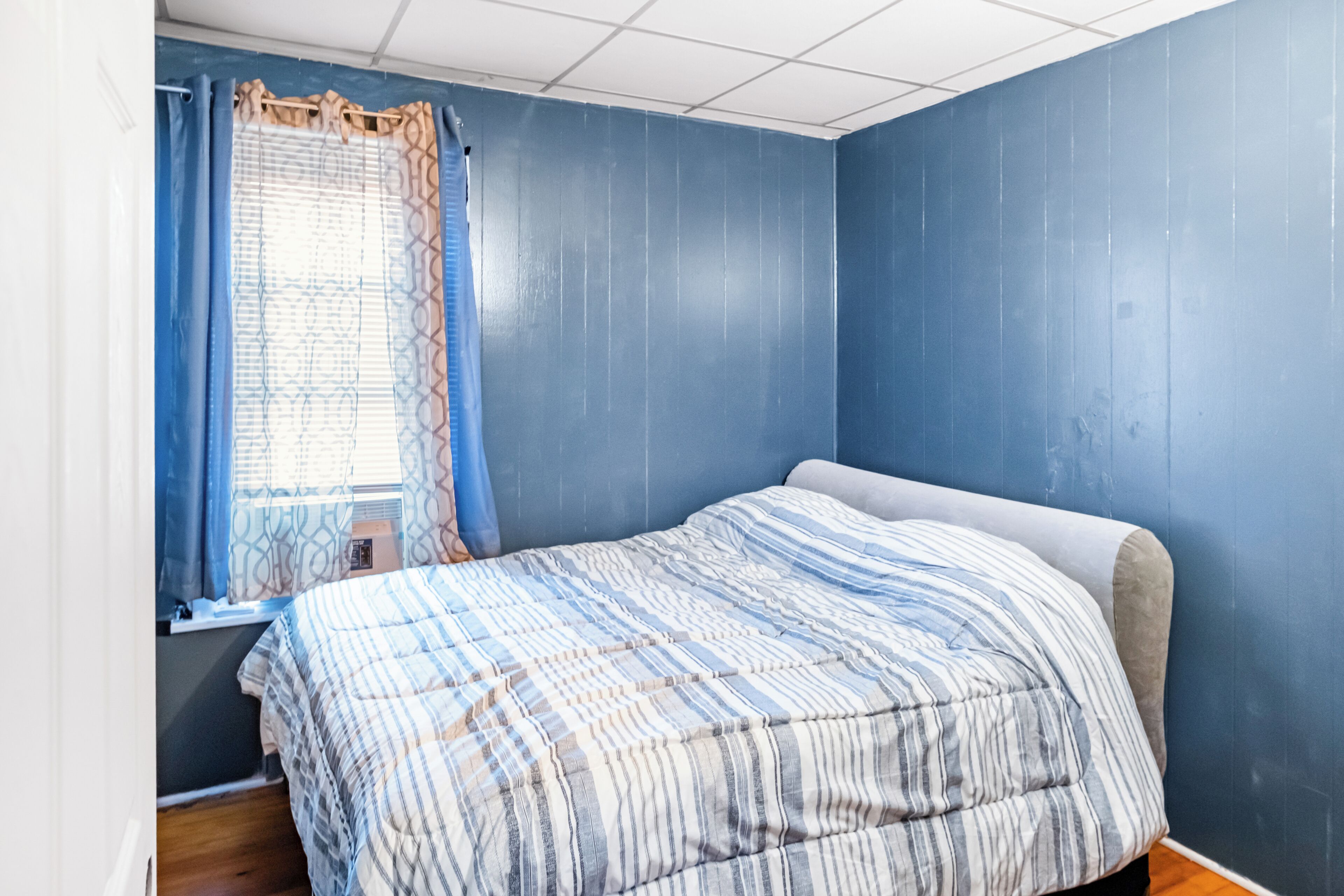 Ein Schlafzimmer mit einem Bett, einem Fenster mit Vorhängen und blauen Wänden.