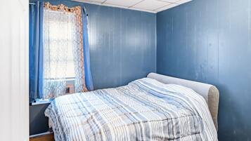 Een slaapkamer met een bed, een raam met gordijnen en blauwe wanden.