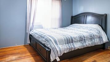 Un lit simple avec une tête de lit sombre, dans une pièce aux murs bleu clair et au plancher en bois.