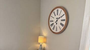 Une pièce avec un bureau en bois, une chaise noire, une horloge murale et une lampe.