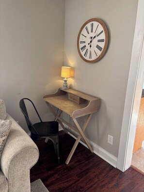 A room with a wooden desk, a black chair, a wall-mounted clock, and a lamp.