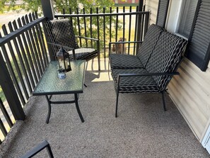 A balcony with a glass table and two chairs, a lantern, and a small potted plant.