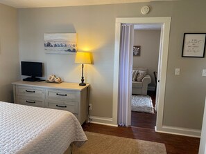 A bedroom with a bed, a desk with a lamp, a television, and a door leading to a bathroom. - Cozy Upstairs 2BR Apartment Near Hospitals & Charleston (Saint Albans)