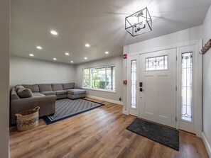 A living room with a sectional sofa, a patterned rug, and a wooden floor.