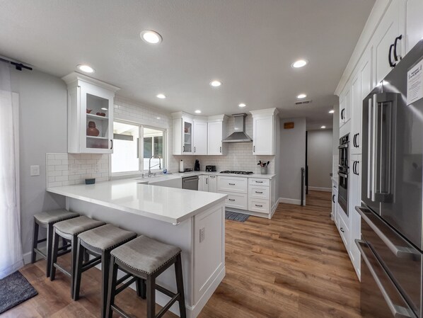 A modern kitchen with white cabinetry, a large island with stools, and stainless steel appliances.