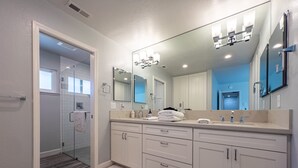 A modern bathroom with a walk-in shower, a large mirror, and a vanity with a double sink.