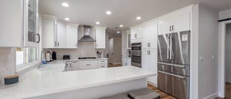 Una cocina moderna con armarios blancos, electrodomésticos de acero inoxidable y una isla central con taburetes de bar.