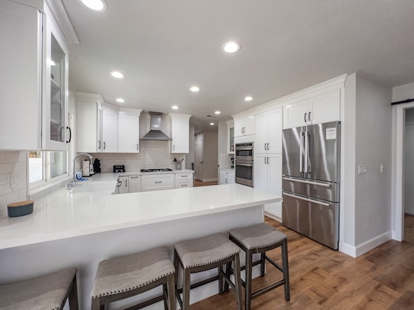 A modern kitchen with white cabinetry, stainless steel appliances, and a central island with bar stools.