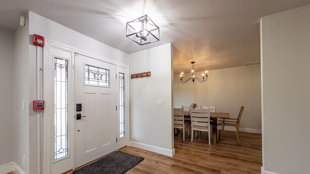 A hallway with a wooden floor, a door with a fire alarm, and a dining area with a chandelier.