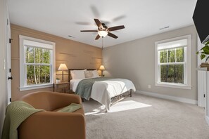 Une chambre à coucher avec un lit, deux tables de chevet, un ventilateur de plafond et de grandes fenêtres.