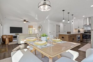 Une cuisine moderne équip ée d’appareils électroménagers en acier inoxydable, un coin repas avec une table en bois pour quatre personnes et un ventilateur de plafond.