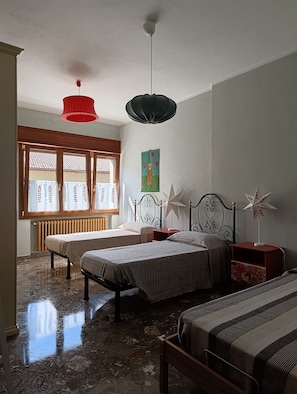 Camera da letto con due letti, un termosifone, una finestra con tende, una ventola a soffitto e una lampada a parete.