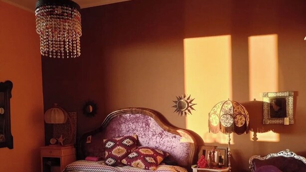 Quarto com cama, mesa de cabeceira, abajur, cadeira e um objeto decorativo na parede.
